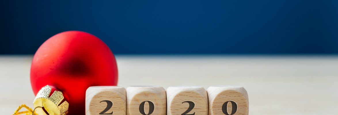 Red holiday bauble next to wooden dices with 2020 sing. Over navy blue background.