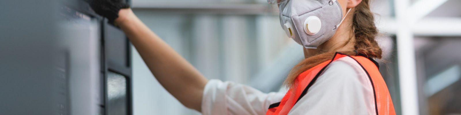 Female Engineer wear face mask with safety vest and yellow helmet operating control CNC Machinery at factory Industrial